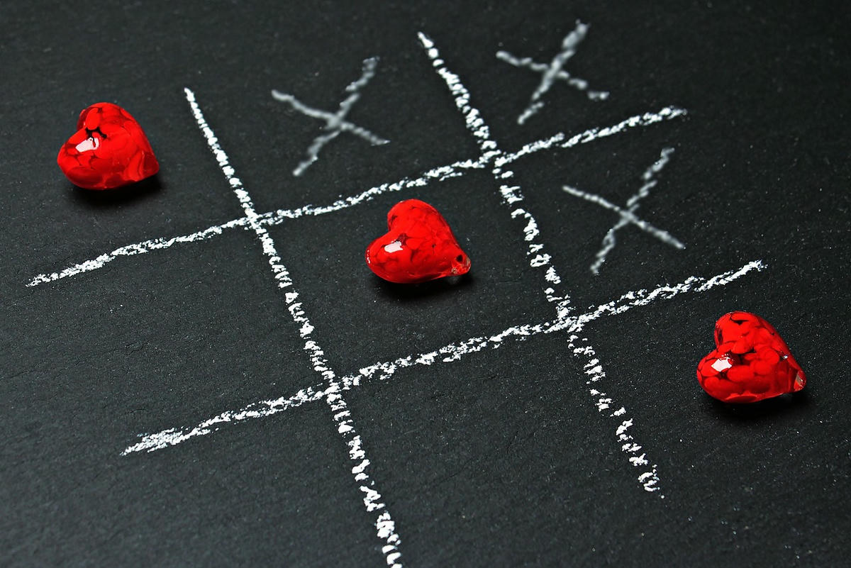 Tic-tac-toe spel met rode harten en kruisen op zwart bord – symbool voor keuzes, eerlijkheid en de strijd om persoonlijke autonomie.