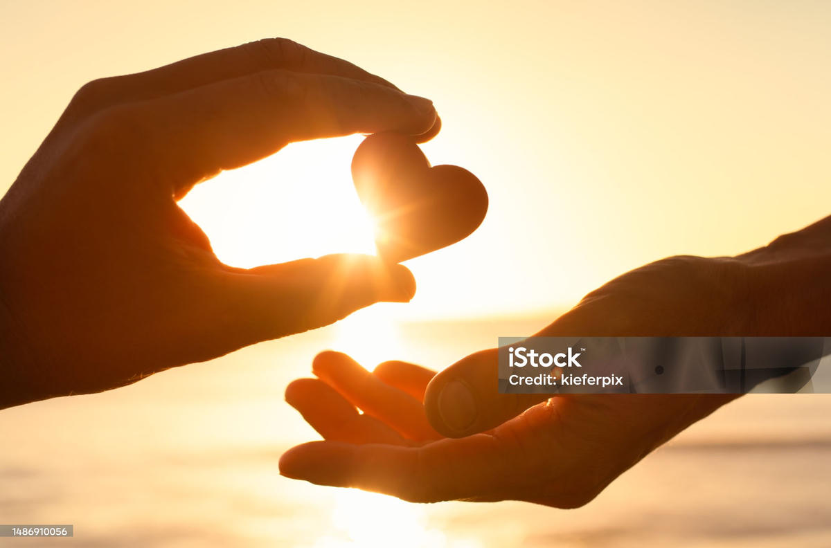 Man geeft hartje in handen van vrouw bij zonsondergang – symbool voor liefde en aantrekkingskracht