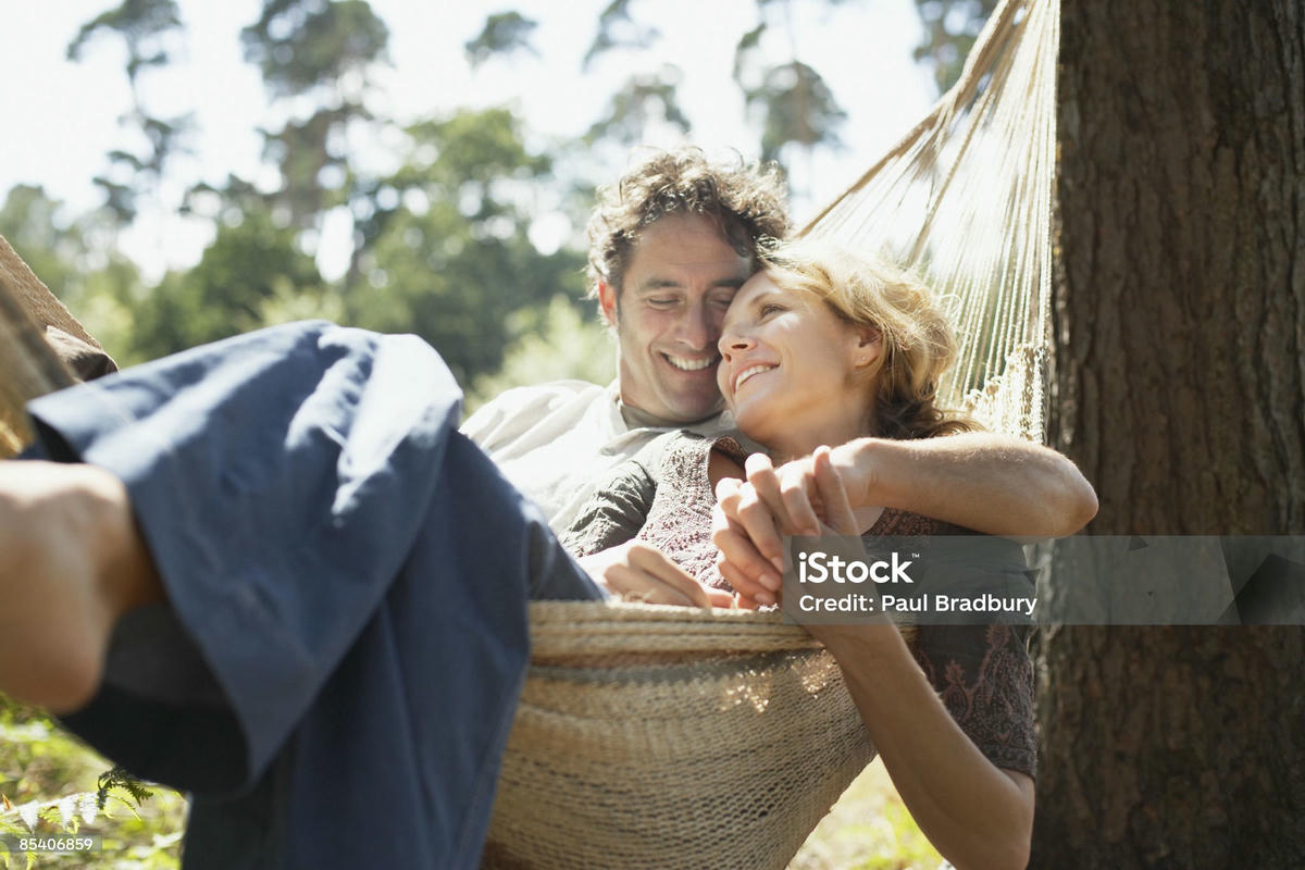 Koppel ontspant samen in een hangmat in de natuur, genietend van een rustig moment van verbondenheid en intimiteit.