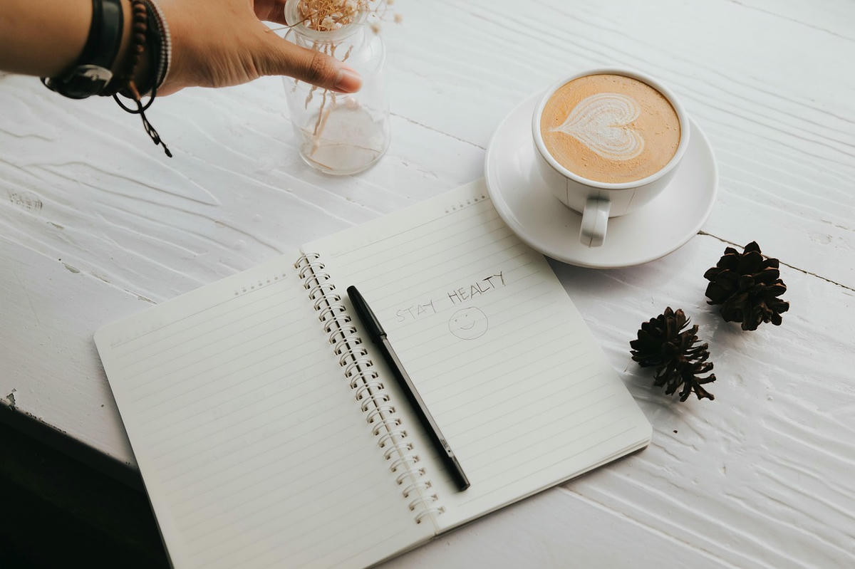 Letterbord met tekst “Love will lead the way” naast een cappuccino met hartje en een notitieboek — symbool voor routine, persoonlijke groei en liefde.