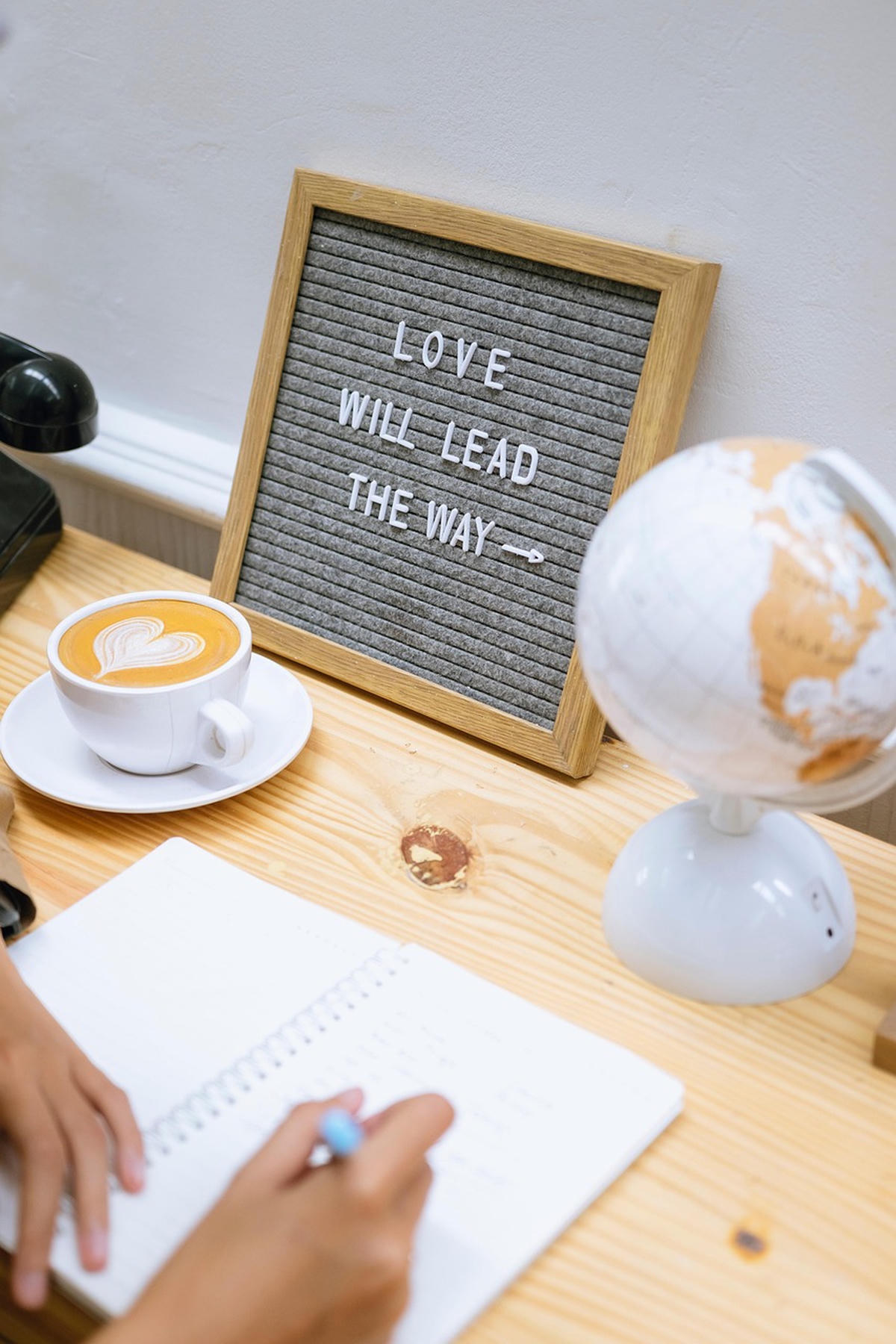 Letterbord met tekst "Love will lead the way", naast een koffie met hartje en een notitieboek – symbool voor liefde, routine en persoonlijke groei.