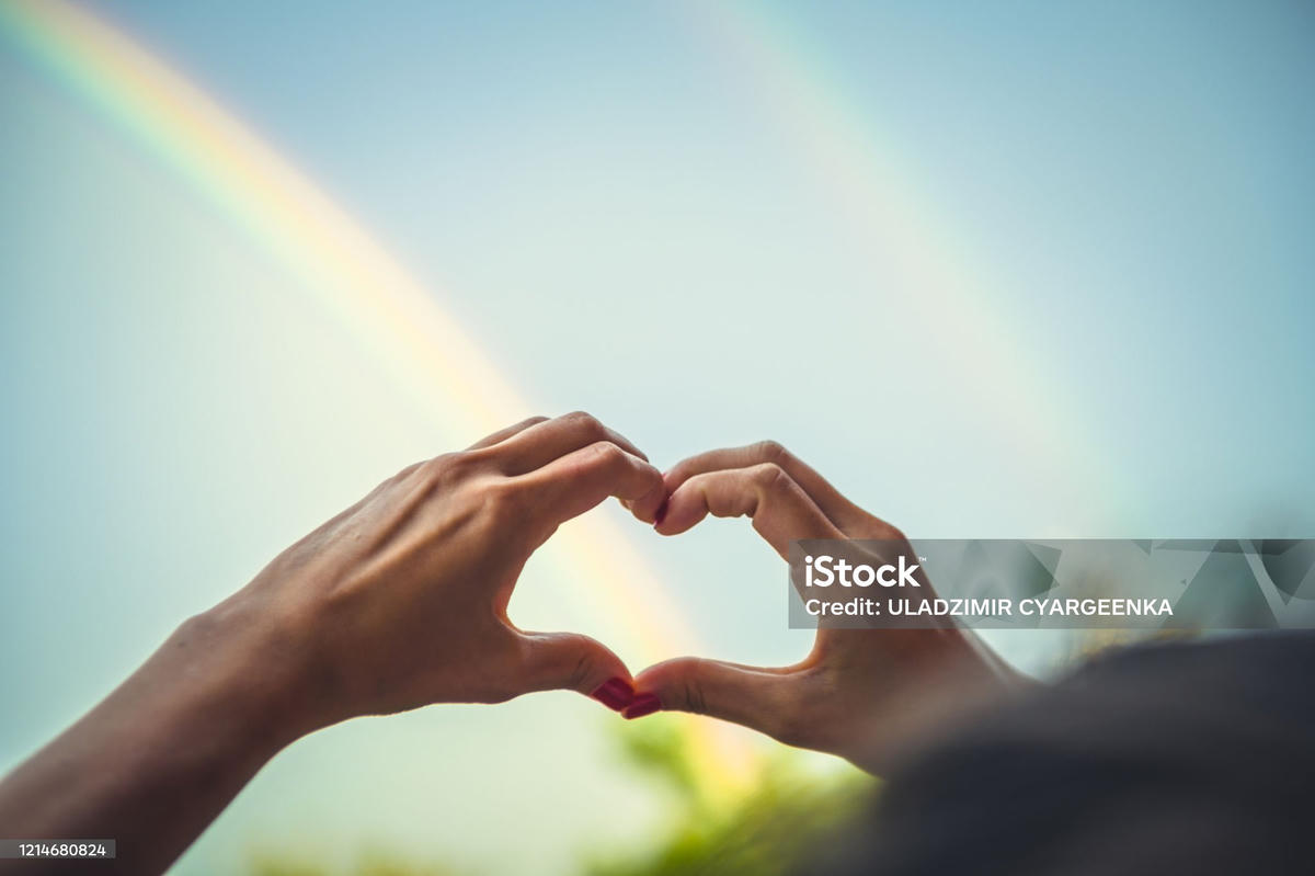 Handen in hartvorm voor een dubbele regenboog – symbool voor liefde, diversiteit en queerplatonic verbindingen buiten traditionele romantiek