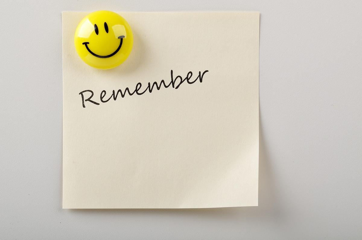Een gele post-it met het woord “Remember” erop geschreven, vastgehouden door een ronde smiley-magneet — symbool voor zelfbewustzijn, positieve energie en het herinneren van je ware kracht.