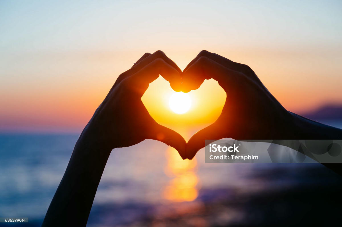 Handen vormen een hart rond de ondergaande zon boven zee – symboliseert romantische fantasiewerelden.