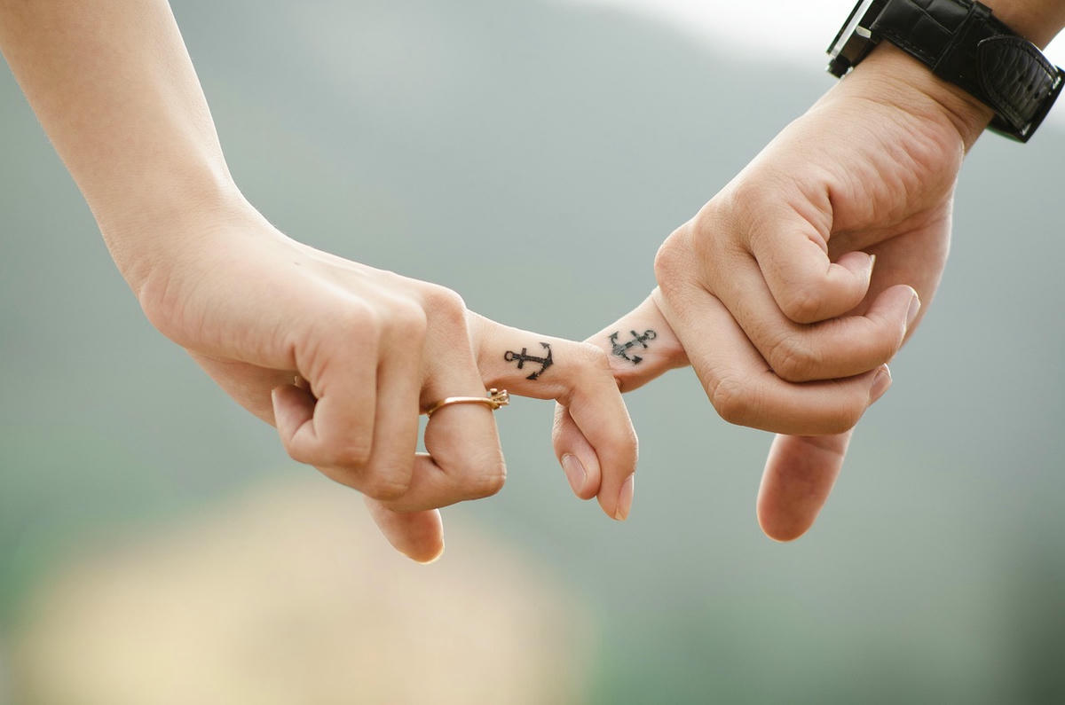 Handen met anker-tatoeages die vingers verstrengelen – symbool van liefde, vertrouwen en moderne relatievormen zoals open relaties en de strijd tegen gaslighting.